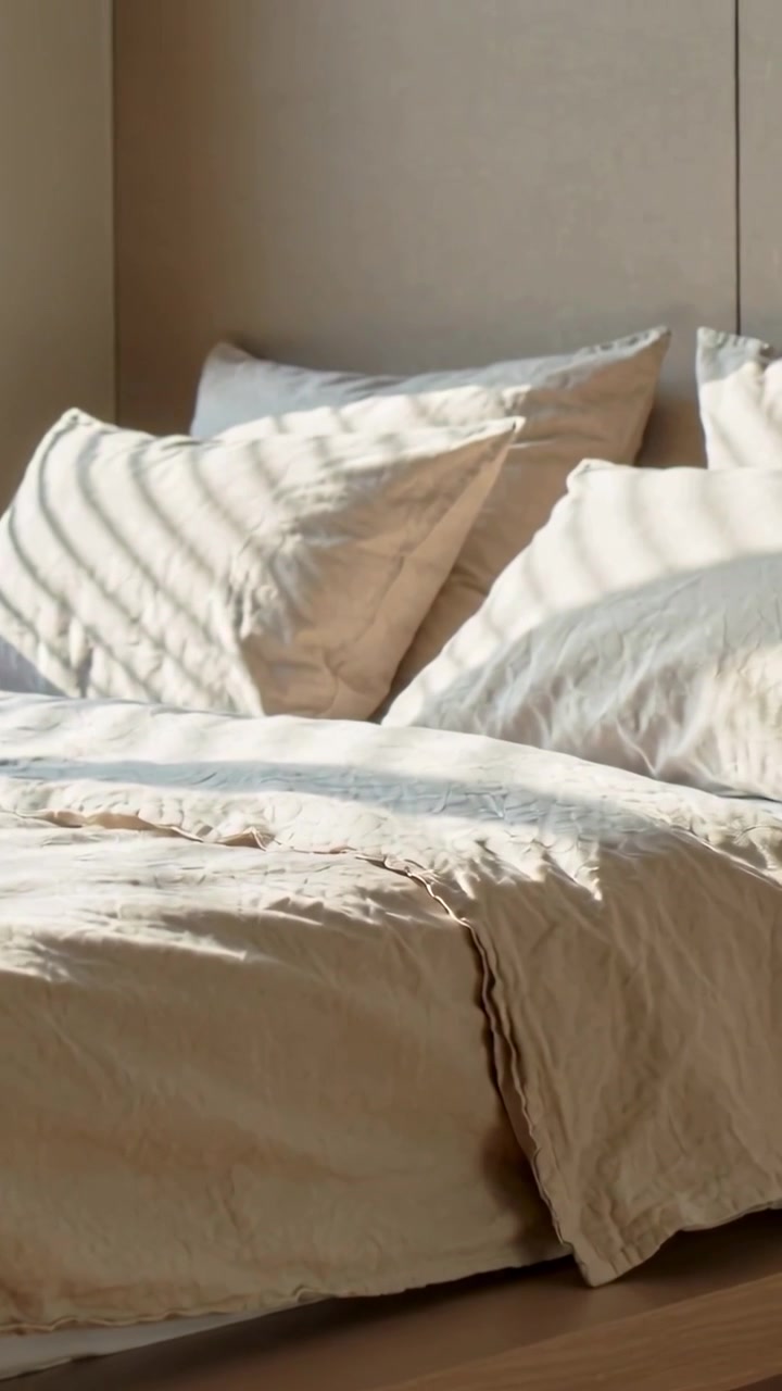 Video verticale: Panoramica di un letto in camera da letto mentre la luce che filtra attraverso le persiane si muove su cuscini e plaid.