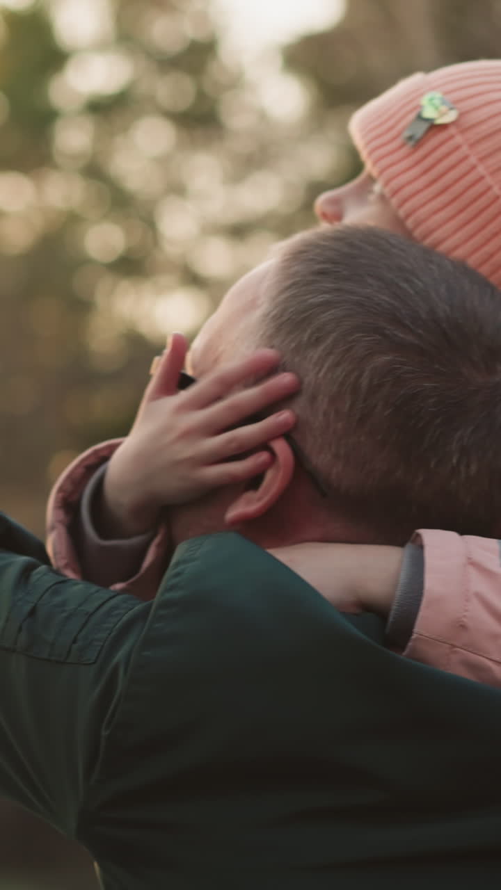 un hombre con una chaqueta verde lleva a su hija, que está vestida con una chaquita rosa y un gorro a juego, en sus hombros. la niña coloca su mano suavemente en su cara mientras señala hacia el cielo