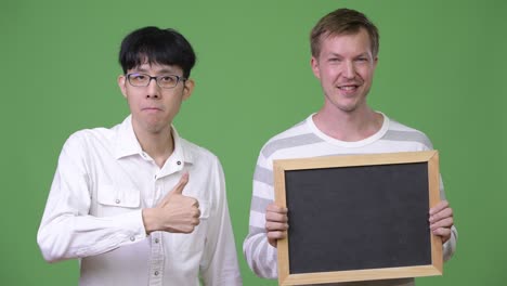 two happy young multi-ethnic businessmen showing blackboard and giving thumbs up