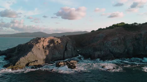 panorámica aérea de grandes acantilados costeros y olas con drones al atardecer