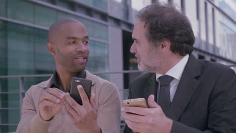 hombres profesionales teniendo una discusión sobre la reunión con teléfonos inteligentes cerca del edificio de oficinas