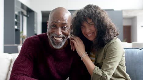 Retrato-De-Una-Feliz-Pareja-Birracial-Sentada-En-El-Sofá-Y-Haciendo-Videollamadas-En-Casa,-Cámara-Lenta