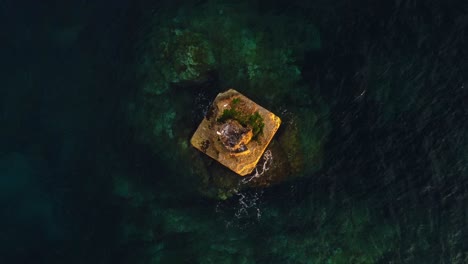 bird's eye view of offshore squared rock with seagulls flying over, aerial