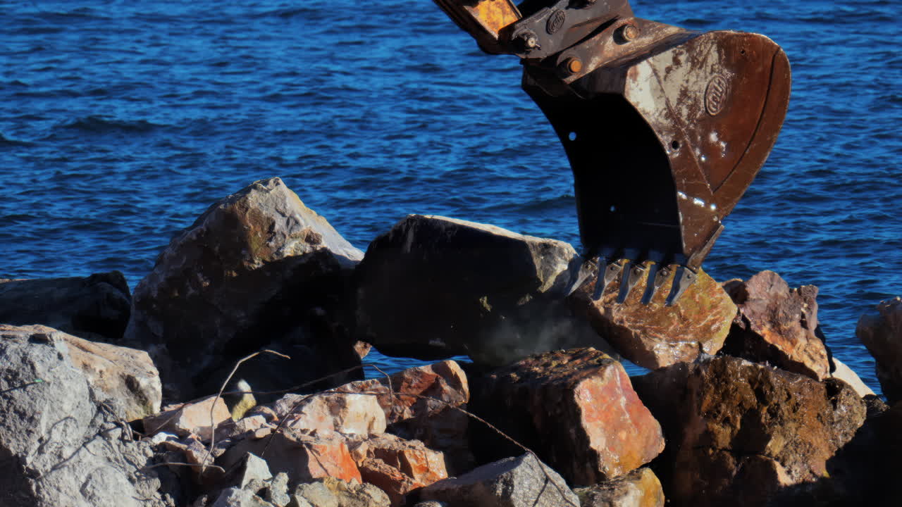 A large, yellow and rusty excavator picking up rocks and water from the sea