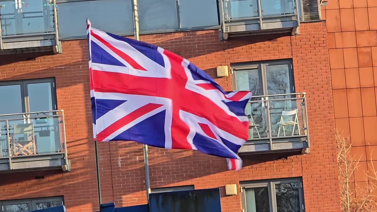 Medium shot of flag of the United Kingdom waving in the wind in front of a building during the day, outdoor