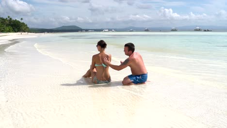 man putting a back women sunscreen by the sea