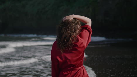 A-woman-in-a-red-robe-walks-along-the-Seixal-beach-in-Madeira-during-sunset-with-cliffs-in-the-background