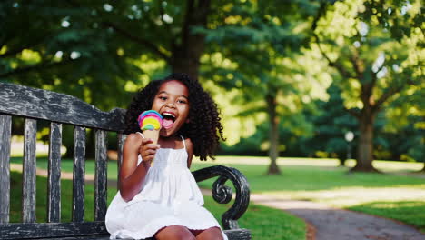 happy little girl enjoying a rainbow ice cream cone in a park