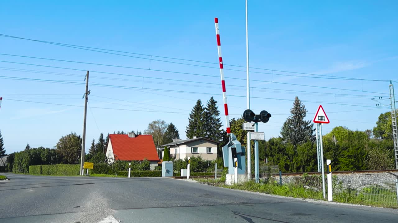 Railway or a railroad crossing in Laagri Estonia during summer time while boom gate is up and cars are driving in slow motion over railroad. Sun is shining and sky is blue, trees in the background.