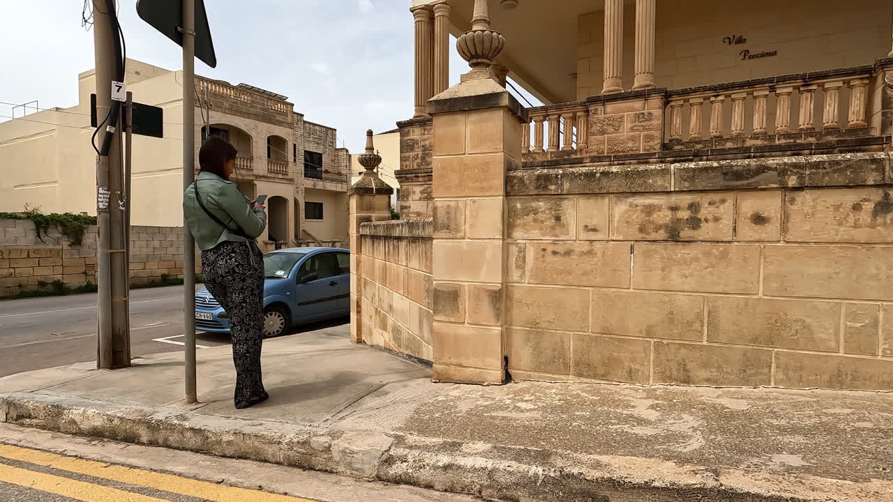 Donna in piedi all'angolo di una strada a Malta che usa il telefono e guarda verso la fotocamera