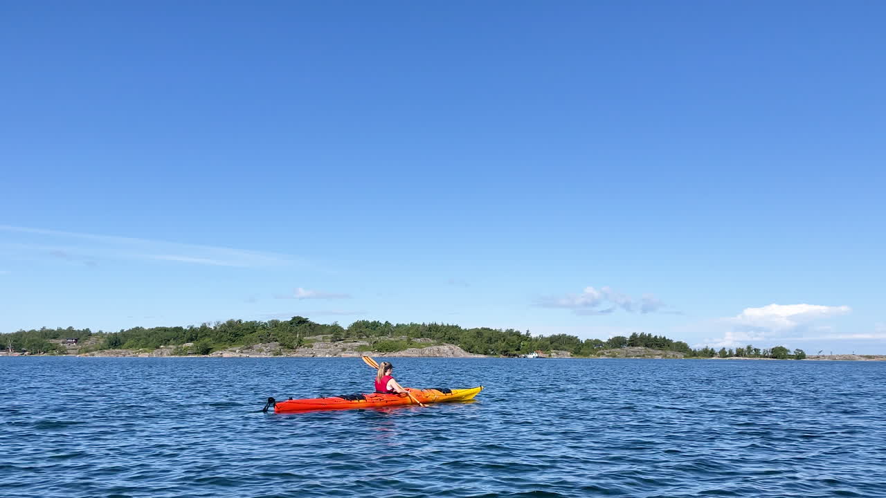 mujer en un kayak remando hacia la isla en aguas abiertas