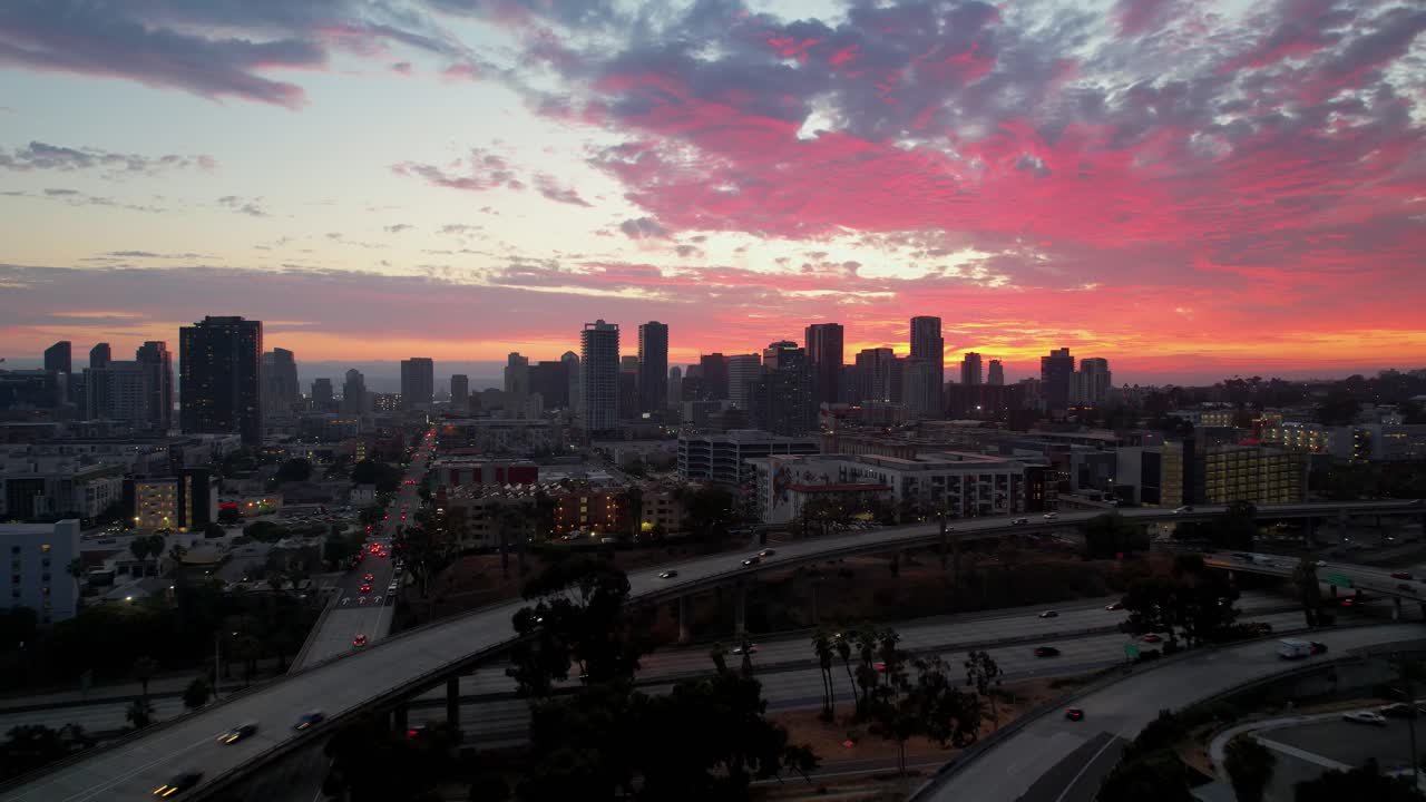 Dron volando hacia el centro de San Diego, deslizándose sobre el tráfico de la autopista a las 8 PM con cálida luz de atardecer y movimiento urbano.