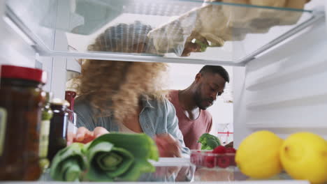 vista mirando desde el interior del refrigerador como pareja puerta abierta y desempaques bolsa de compras de alimentos