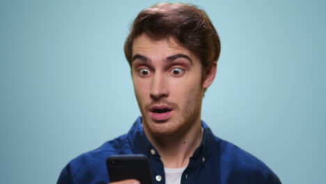 excited man using smartphone in studio. student reading news on phone screen