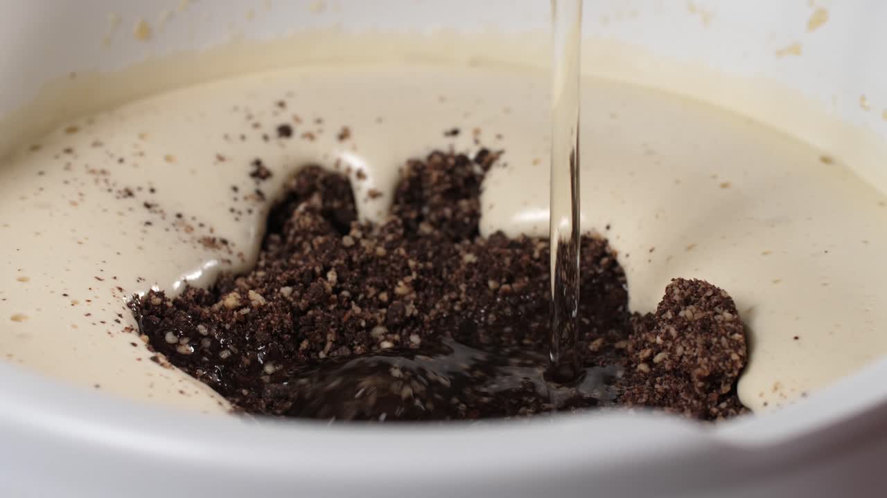 Preparare una torta al cioccolato e mandorle senza glutine e senza farina, versare olio di cocco liquido in una ciotola bianca con uova sbattute e ingredienti secchi come mandorle macinate e pezzi di cioccolato