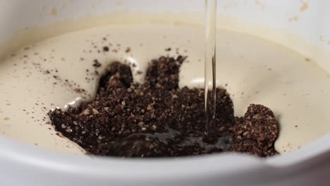 haga un pastel de chocolate con almendras sin harina y sin gluten, vierta aceite de coco líquido en un tazón blanco con huevos batidos e ingredientes secos como almendras molidas y trozos de chocolate