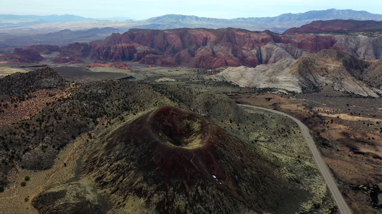 A circling view of an extinct volcano in a desert valley surrounded by mountains and a road with a passing cars