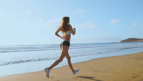 beautiful woman in sports shorts and t-shirt running on the beach with white sand and blue ocean water on the island in slow motion. waves and sand hills on the back won