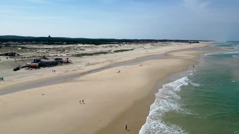 Gente-Disfrutando-De-La-Playa-En-Biscarrosse-Francia-Con-Olas-Y-Restaurante-Junto-Al-Mar,-Plano-Aéreo-A-La-Derecha