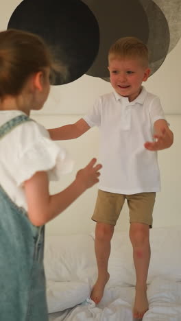 children play actively on bed at glamping. smiling little boy catches sister hands hopping on mattress in bedroom. happy kids in tent on vacation