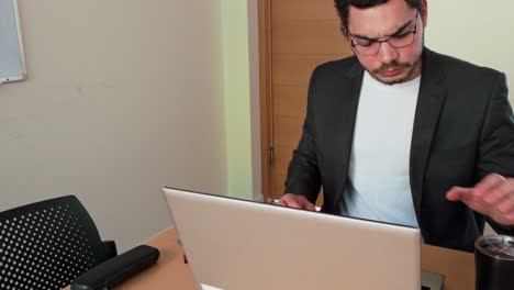 Diligent young man crunching numbers using a graphing calculator and laptop in an office setting.