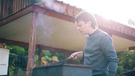 young man standing near the summer house prepares the coals in the grill fanning them