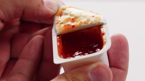 hand opening a packet of chili sauce