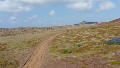 Drone-Vista-Pájaros-Ojo-De-Jinete-Conduciendo-Motocicleta-Entre-Un-Acantilado-Verde-En-Islandia.-Vista-Aérea-Siguiendo-Al-Hombre-Motocross-Sobre-Groenlandia