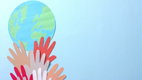 close-up van handen samen met een globe gemaakt van kleurrijk papier op blauwe achtergrond met kopieerruimte