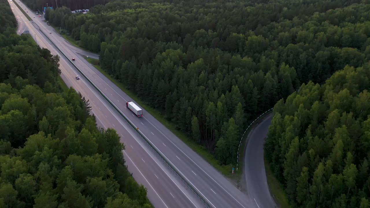 도시 지평선에 있는 숲 속의 도로에서 트럭이 달린다. 드론에서 볼 때, 직선 도로가 도시의 지평선 위에 놓여 있다.