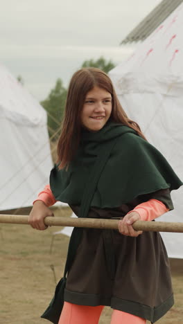 smiling teenage girl and young man train to fight on spears near white tents. medieval youth improve fighting skills in preparation for military campaign