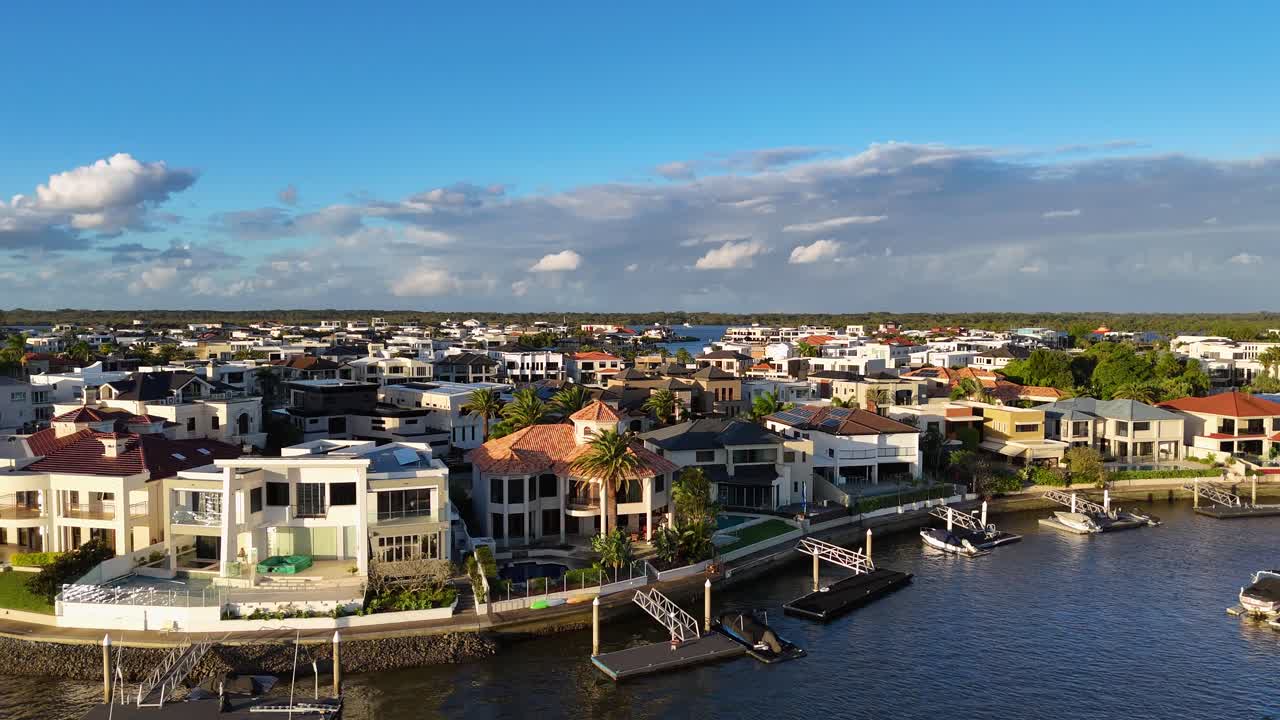 Drone captures stunning views of luxury waterfront homes with vibrant skies and serene waters, showcasing architectural elegance and natural beauty