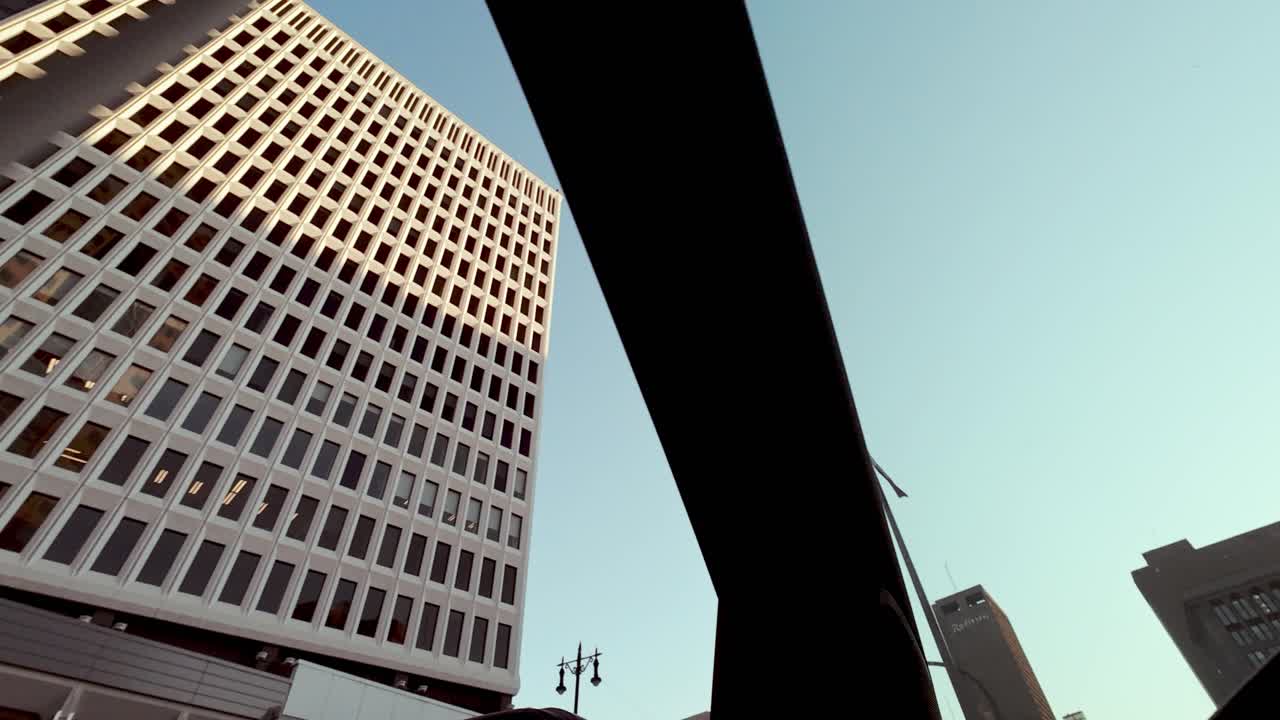 POV shot from inside a moving car looking up at skyscraper peaks against a bright blue sky