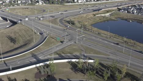 aerial early morning over sunny summer highway freeway exit enterance to the connector of the main city hub from residention to commercial avenues around cookie cut homes man made artifical pond 1-3