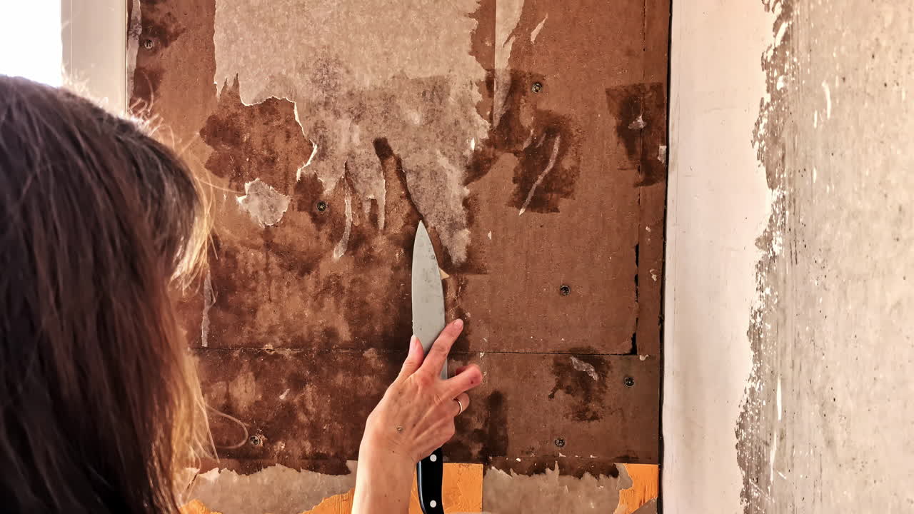 Ristrutturazione del muro in corso mentre una donna rimuove la carta da parati con una spatola
