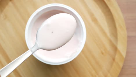 coge el yogur con una cuchara de un recipiente de plástico,