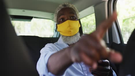 african american senior man wearing face mask pointing towards a direction while sitting in the car