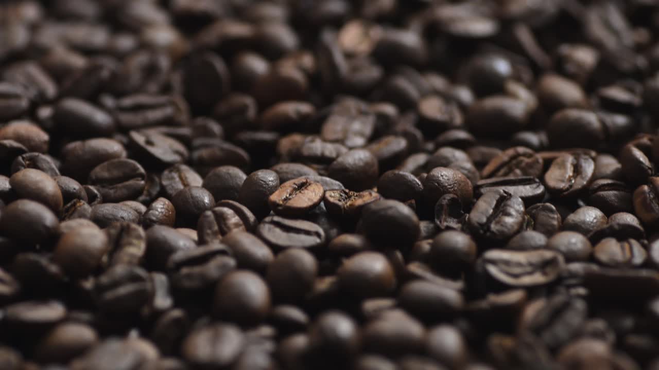 Primo piano dettagliato di chicchi di caffè tostati con una texture scura e intensa. La telecamera si muove sopra i chicchi di caffè.