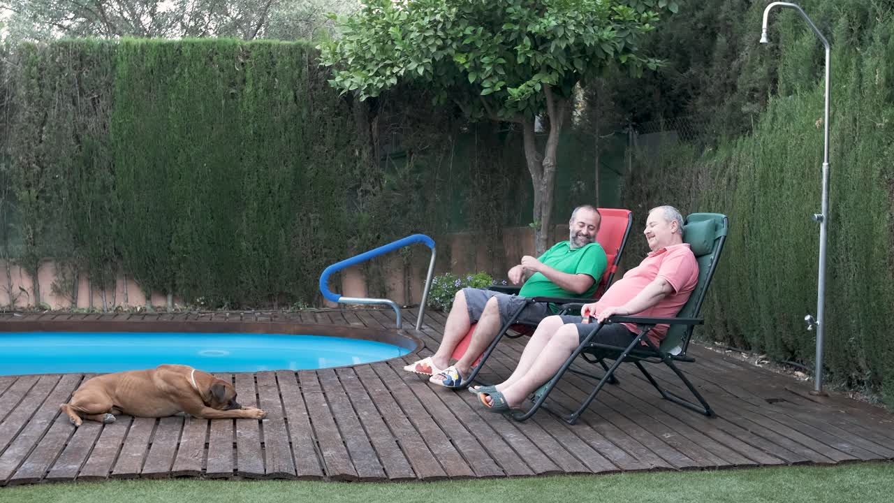 Two men relaxing by the pool with their dog