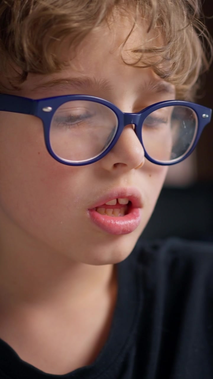 Giovane ragazzo con gli occhiali che si concentra nello scrivere i compiti