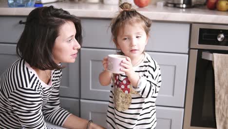 Madre-Le-Da-A-Su-Hija-Un-Vaso-De-Agua,-La-Niña-Bebe,-Mamá-Sonríe-En-La-Cocina