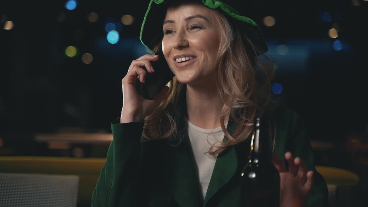 Portrait Of Blonde Woman Using A Smartphone, Drinking A Beer And Wearing An Irish Green Hat