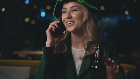 Retrato-De-Mujer-Rubia-Usando-Un-Teléfono-Inteligente,-Bebiendo-Una-Cerveza-Y-Usando-Un-Sombrero-Verde-Irlandés