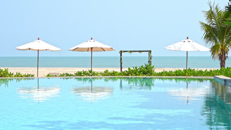 sea view sandy beach resort with sun umbrellas reflecting on empty infinity pool