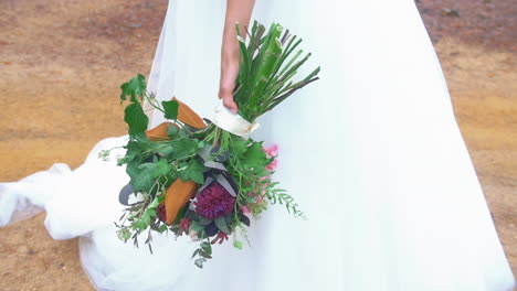 bride in traditional bridal gown holding her colorful bouquet of fresh flowers during outdoor wedding ceremony