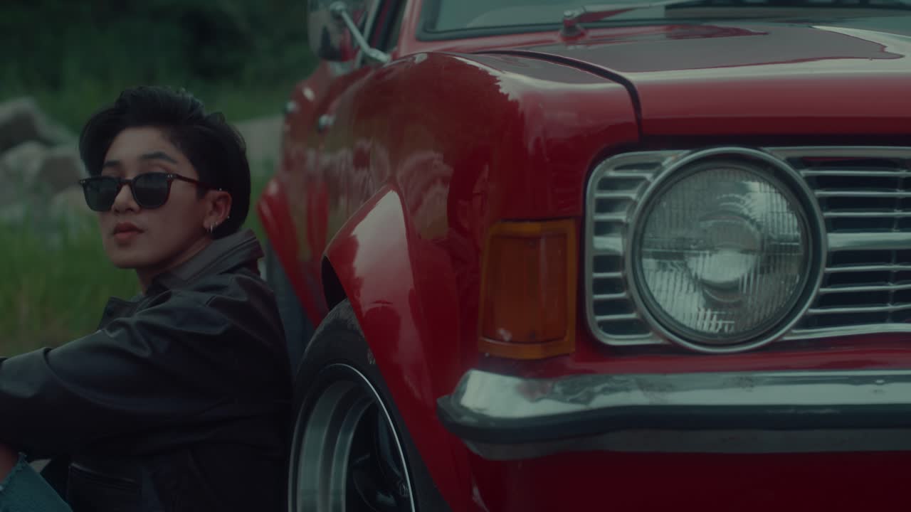 Person sitting next to a classic red car