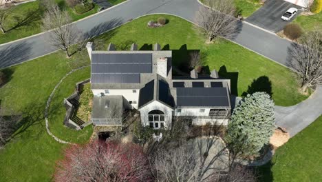 descending aerial above large luxury home with solar panels across roof