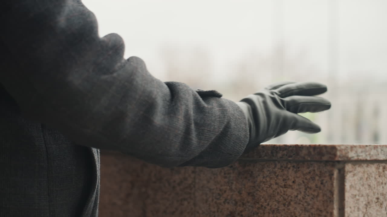 Twórca/projektant testujący granitowy gzyms na zewnątrz, zbliżenie dłoni w rękawiczce sięgającej do kamiennej powierzchni, badającej teksturę i wilgoć, ostrożny gest na polerowanej krawędzi, miejski plac w miękkim rozmyciu.