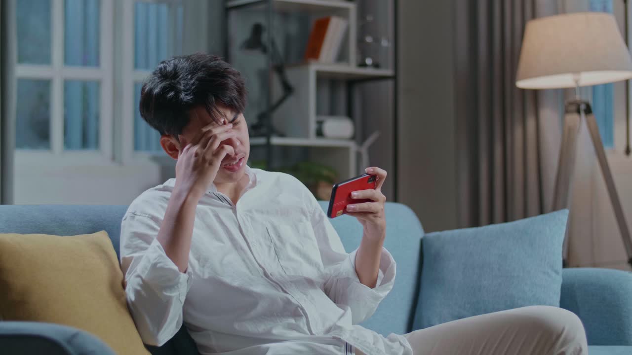 Asian Man Being Upset Losing Game On Smartphone While Sitting On Sofa In The Living Room