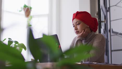 Video-Einer-Konzentrierten-Biracial-Frau-Im-Hijab,-Die-Zu-Hause-Am-Schreibtisch-Sitzt-Und-Am-Laptop-Arbeitet